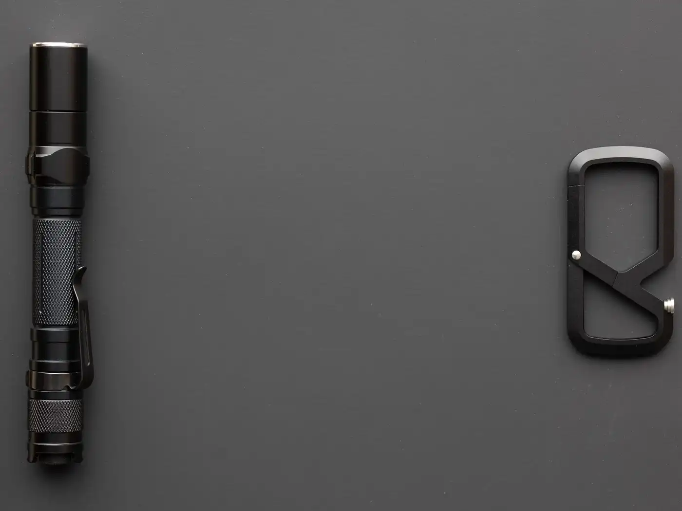 A black aluminium torch and a matte black clip lying on a dark grey surface