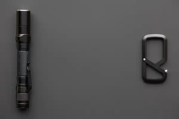 A black aluminium torch and a matte black clip lying on a dark grey surface