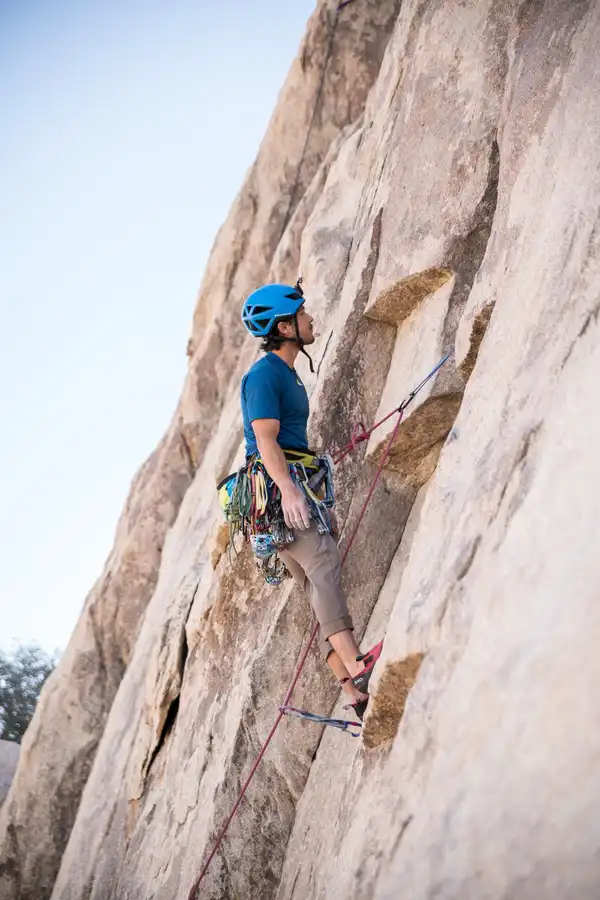A climber in a blue helmet and harness leads up a steep pale rock face