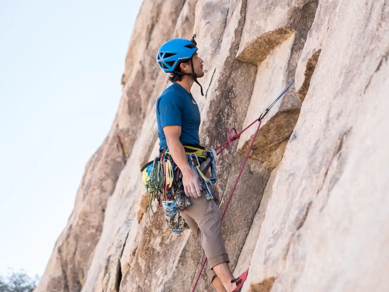 A climber in a blue helmet and harness leads up a steep pale rock face