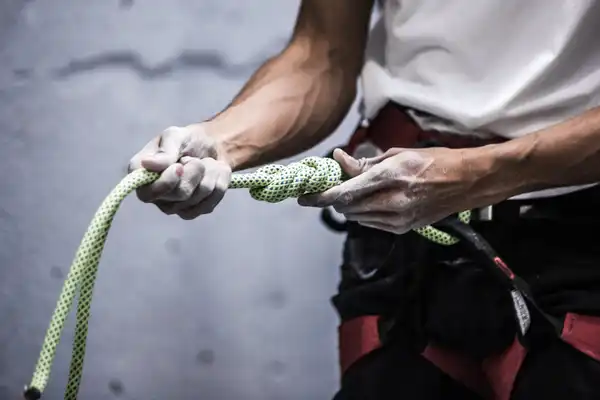 A climber in a harness ties a figure-eight knot in a pale green rope