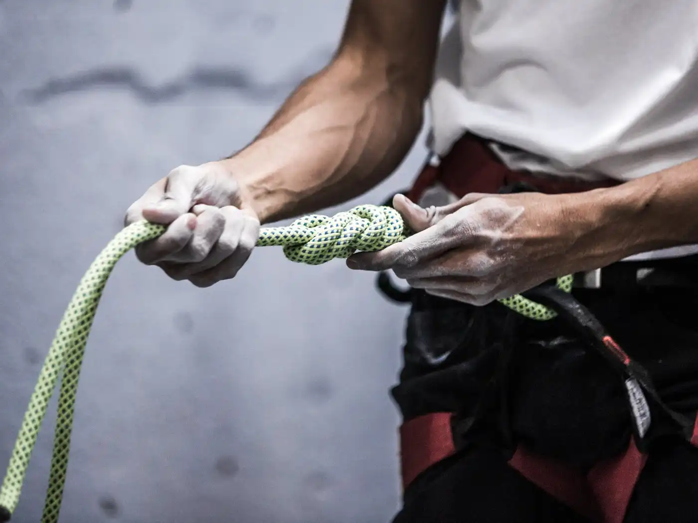 A climber in a harness ties a figure-eight knot in a pale green rope