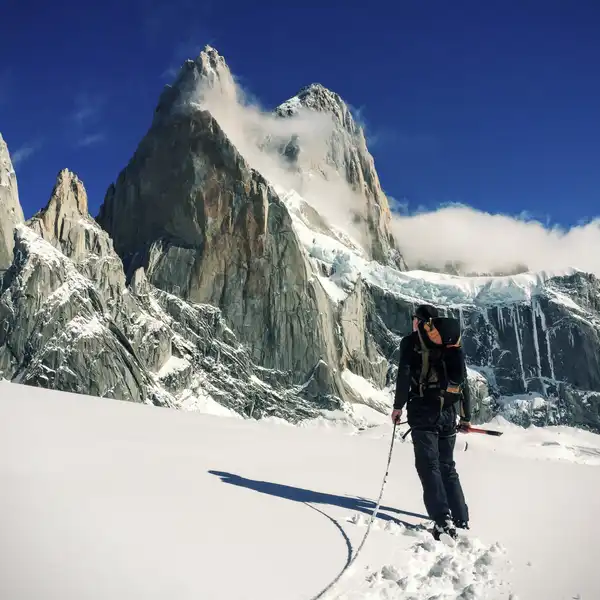 A ski tourer with poles walks across a snowfield toward jagged granite peaks
