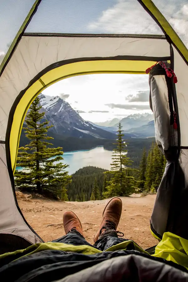 The view from inside a tent: boots at the open door and a turquoise mountain lake below